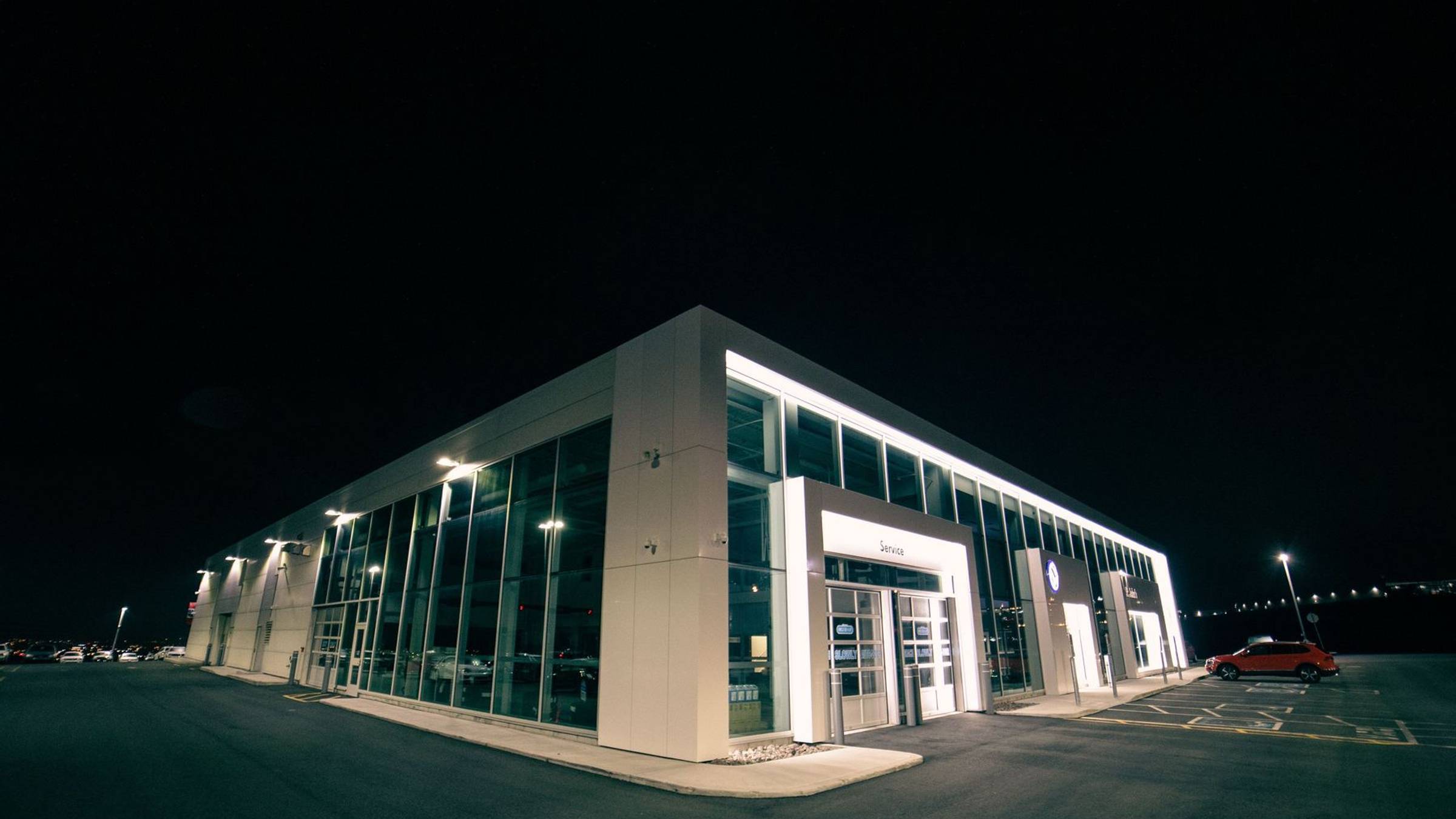 Gewerbeobjekt mit beleuchteter Fassade und geparkten Fahrzeugen bei Nacht